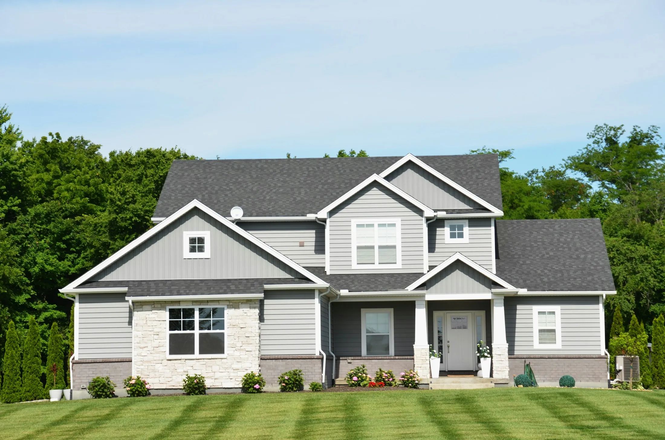 A gray family home with multiple shingle roof planes, white gable trim and a green lawn.