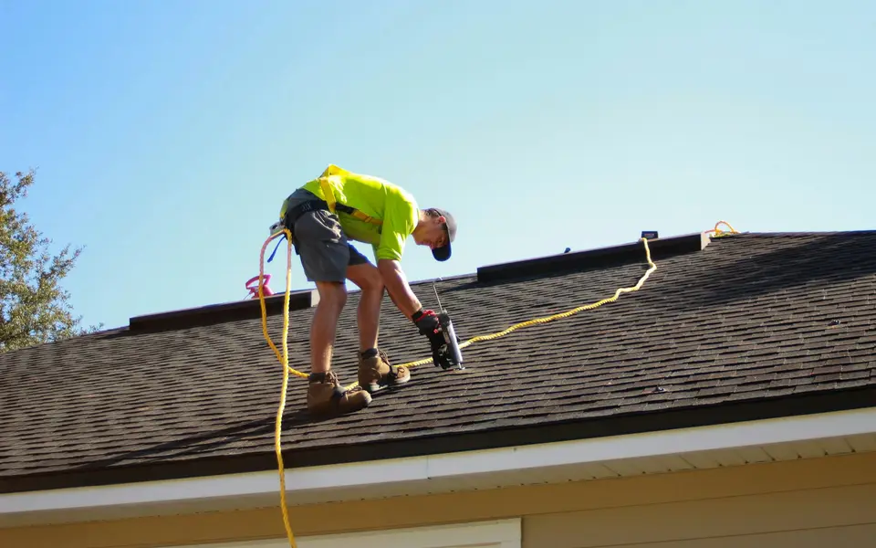A roofer checking a shingle roof beneath a wide blue sky.