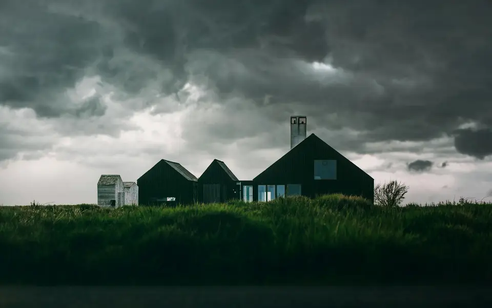 Dark storm clouds gathering over a farmhouse and a field.